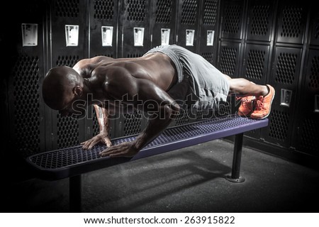 Portrait of a lean toned and ripped muscle fitness man doing push ups on a locker room bench under dramatic low key lighting.