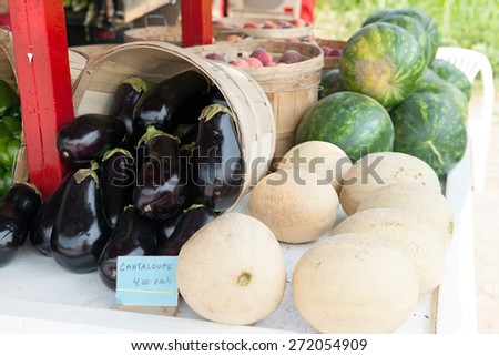 Fresh melons for sale at a farm stand along with some fresh eggplants.  Shallow depth of field.