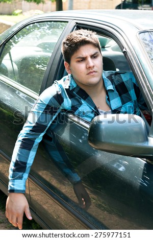 An irritated young man driving a vehicle with his head and arm hanging out of the window.