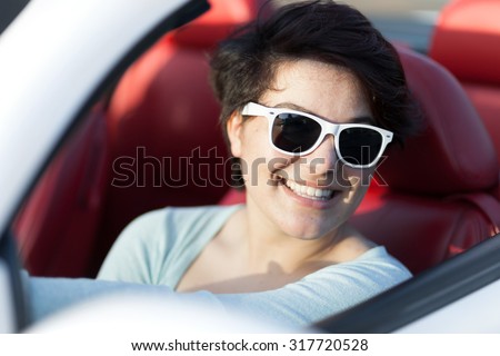 Portrait of smiling woman wearing sunglasses in a convertible sports car with red leather interior.
