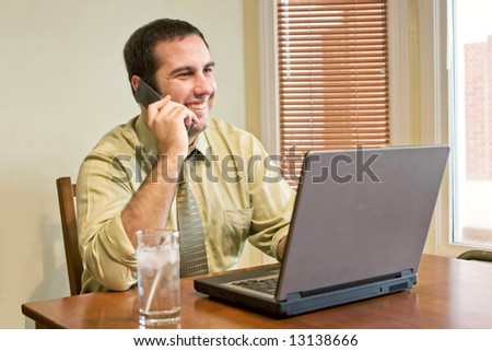 A happy man working from home with his cell phone and laptop.