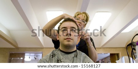 A young man is getting his hair cut by a hairdresser at the salon