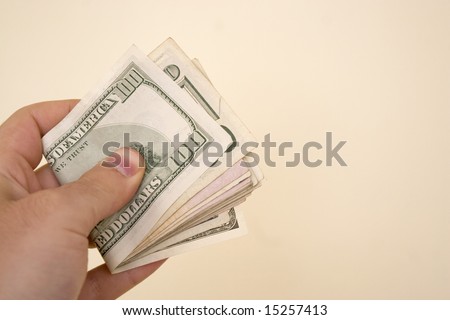A hand holding a big wad of cash isolated over a gold background.