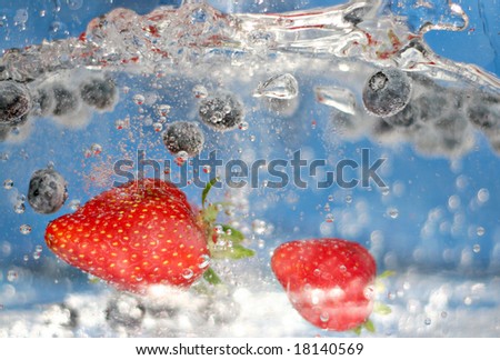 Juicy red strawberries and blueberries plunging into some sparkling water.  Shallow depth of field.