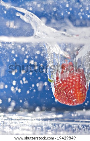 A juicy red strawberry plunging into some water.  Shallow depth of field.