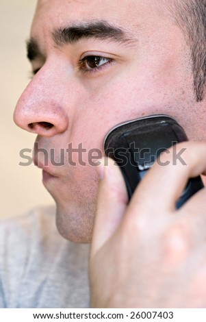 A closeup of a young man shaving his beard off with an electric shaver in black and white.  Shallow depth of field.
