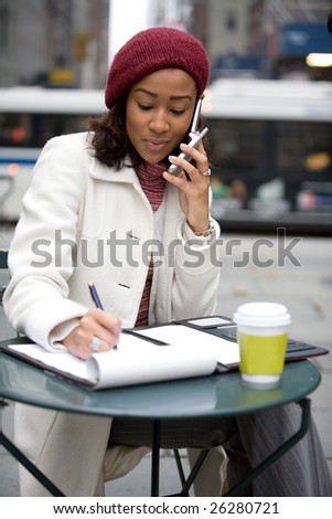 An attractive business woman talking on her cell phone and writing something down in her notes.