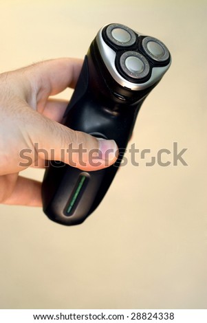 A hand holding an electric shaver isolated over a solid color background.  Shallow depth of field.