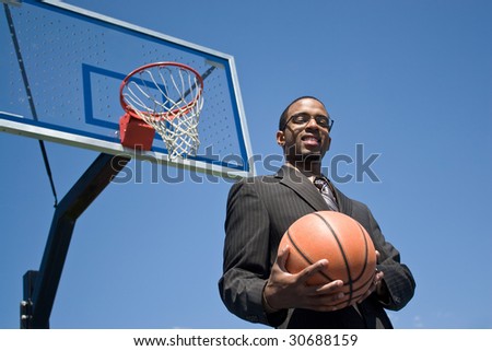 African American man in a business suit posing with a basketball.  He could be a coach player recruiter or trainer.