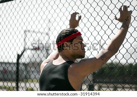 A young basketball leaning up against the chain linked fence at the basketball court.