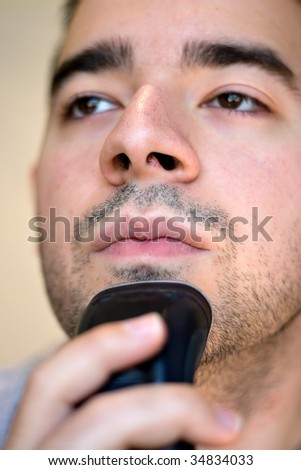 A closeup of a young man shaving his beard off with an electric shaver. Shallow depth of field.