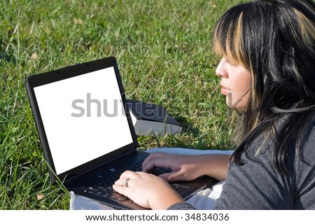 A young student using her laptop computer while laying in the grass on a nice day.  The screen area contains the clipping path.