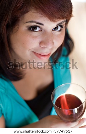 A happy young woman holding a glass of red wine.  Shallow depth of field with focus on the eyes.