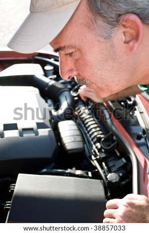 A middle aged man looking under the hood of a car.