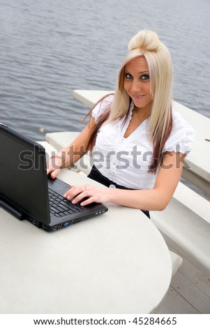 A blonde business woman using a laptop notebook computer outdoors.
