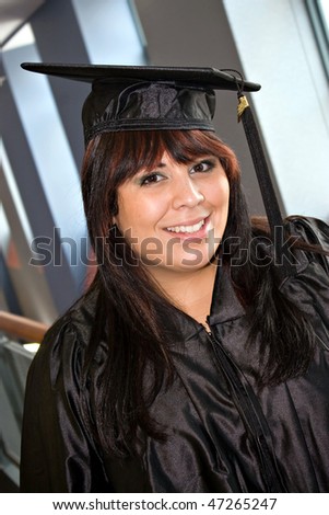 A woman that recently had a school graduation posing in her cap and gown indoors.
