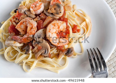 A delicious shrimp scampi dinner with mushrooms and diced tomatoes on linguine pasta.