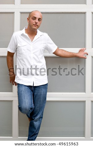 A young man leaning up against a wall hanging out in the city.