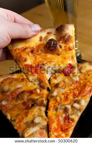 A hand holding a slice of buffalo chicken pizza from the first person point of view.  Shallow depth of field.