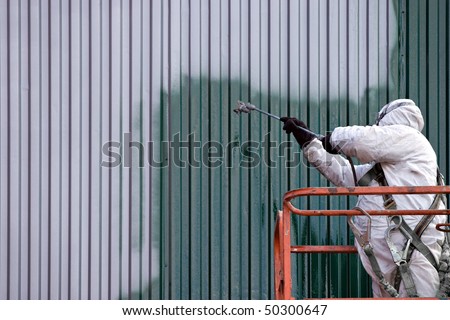 A commercial painter on an industrial lift spray painting a steel exterior wall or duct.