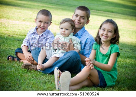A group of four kids with one girl and three boys.  Brothers and sisters getting along nicely.  Shallow depth of field with sharp focus on the boys.
