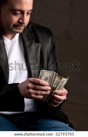 A shady looking man counting a handful of one hundred dollar bills. Shallow depth of field with focus on the money.