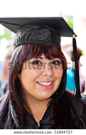 A woman that recently had a university or high school graduation ceremony posing in her cap and gown outdoors.