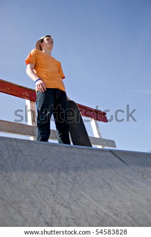 A young man skateboarding standing at the top of a ramp at the skate park prior to attempting a trick.