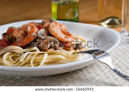 A delicious shrimp scampi pasta dish with mushrooms and diced tomatoes on a white plate. Shallow depth of field.