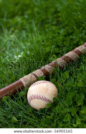 An old wooden baseball bat and ball laying in the green grass with copyspace.  Shallow depth of field.