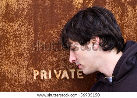 A young man standing outside an old door or entrance that reads PRIVATE.  A great image for any identity theft concept.