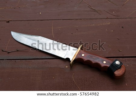 A large bowie knife laying on the wooden table used for hunting or camping.