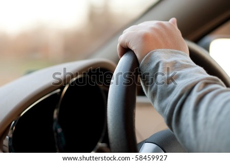 A woman holding the steering wheel of a car with one hand while driving.
