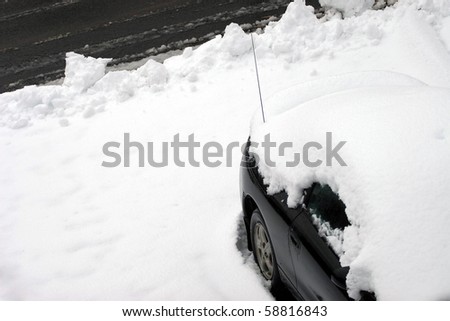 A vehicle covered in snow and snowed in just after the city plow passed the driveway.