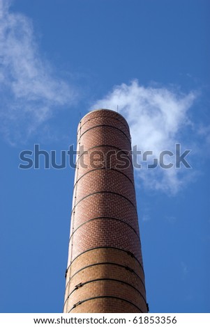 A tall brick factory smoke stack billowing with steam and smoke.