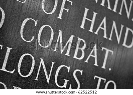 A closeup of the word COMBAT engraved on a war memorial plaque.  Shallow depth of field.