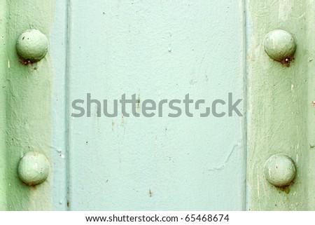 A light green painted metal background texture with four rusted bolts or rivets.