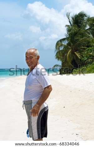 An older Hispanic senior citizen man standing on a tropical beach in the Caribbean.