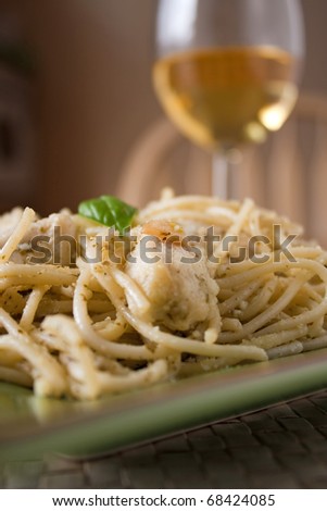 A dish of spaghetti with pesto garlic and chicken with a glass of white wine. Shallow depth of field.