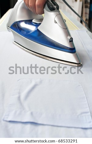 Closeup of and iron pressing and ironing a pocketed dress shirt on an ironing board.