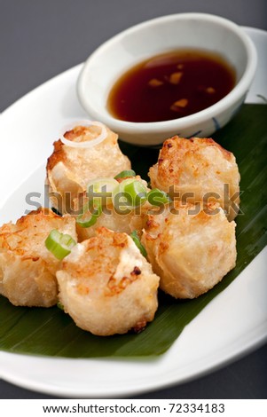 Fried thai appetizers with soy dipping sauce presented on a plate with banana leaf and scallion garnish.