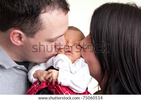 A newborn baby is held by her mother and father as they kiss her cheeks.
