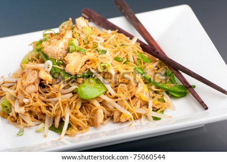 A Thai dish of chicken and noodles stir fry presented on a square white plate with wooden chopsticks.