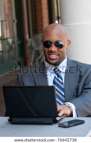 A handsome African American business man in his early 30s working on his laptop or netbook computer with his cell phone nearby.