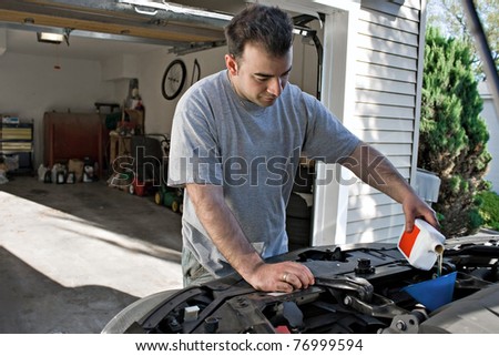 A young man adding oil to his cars engine at the end of an oil change.