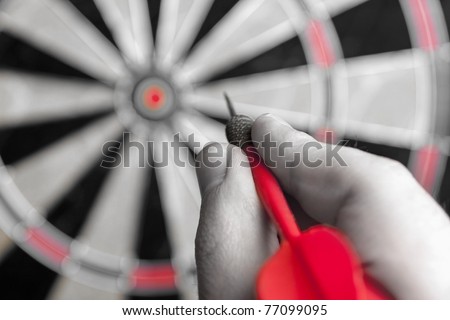 A hand holding a dart getting ready to aim at the dartboard. Shallow depth of field.