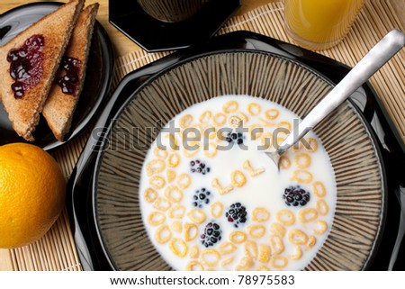 The abbreviation LOL which stands for laughing out loud spelled out of letter shaped cereal pieces floating in a milk filled cereal bowl. Surrounding is an orange juice coffee and toast.