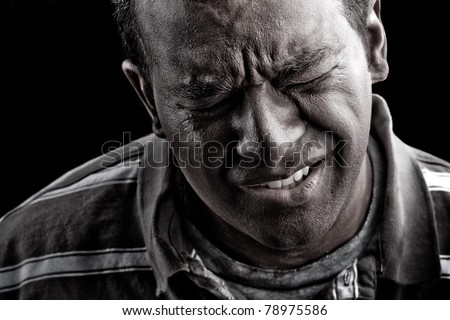 Low key portrait of a man suffering from extreme anguish pain or other hardship over a black background.