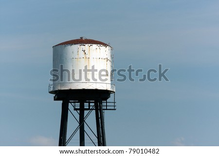 An old rusted water tower isolated over an empty blue sky.