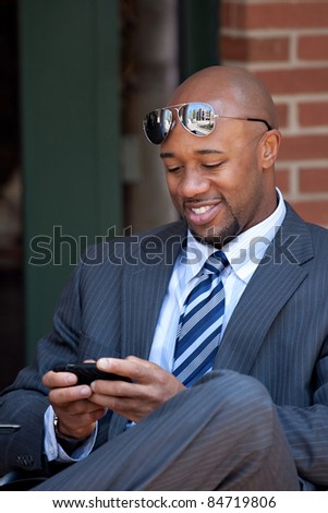 A good looking African American business man works on his smartphone with a smile on his face.